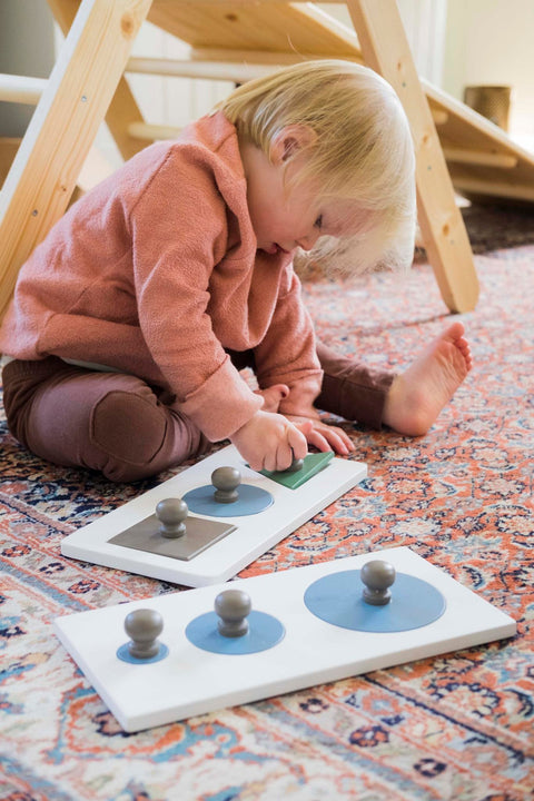 2. Child sitting on patterned rug engaging with Karloova Montessori shape puzzle, concentrating on fitting pieces into board