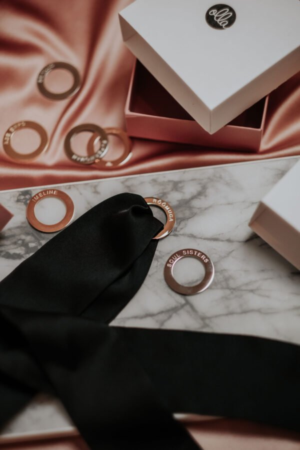 8. Flat lay of Olla Silk Ribbon Bracelet in black with rose gold-plated ring, displayed with branded packaging on satin fabric