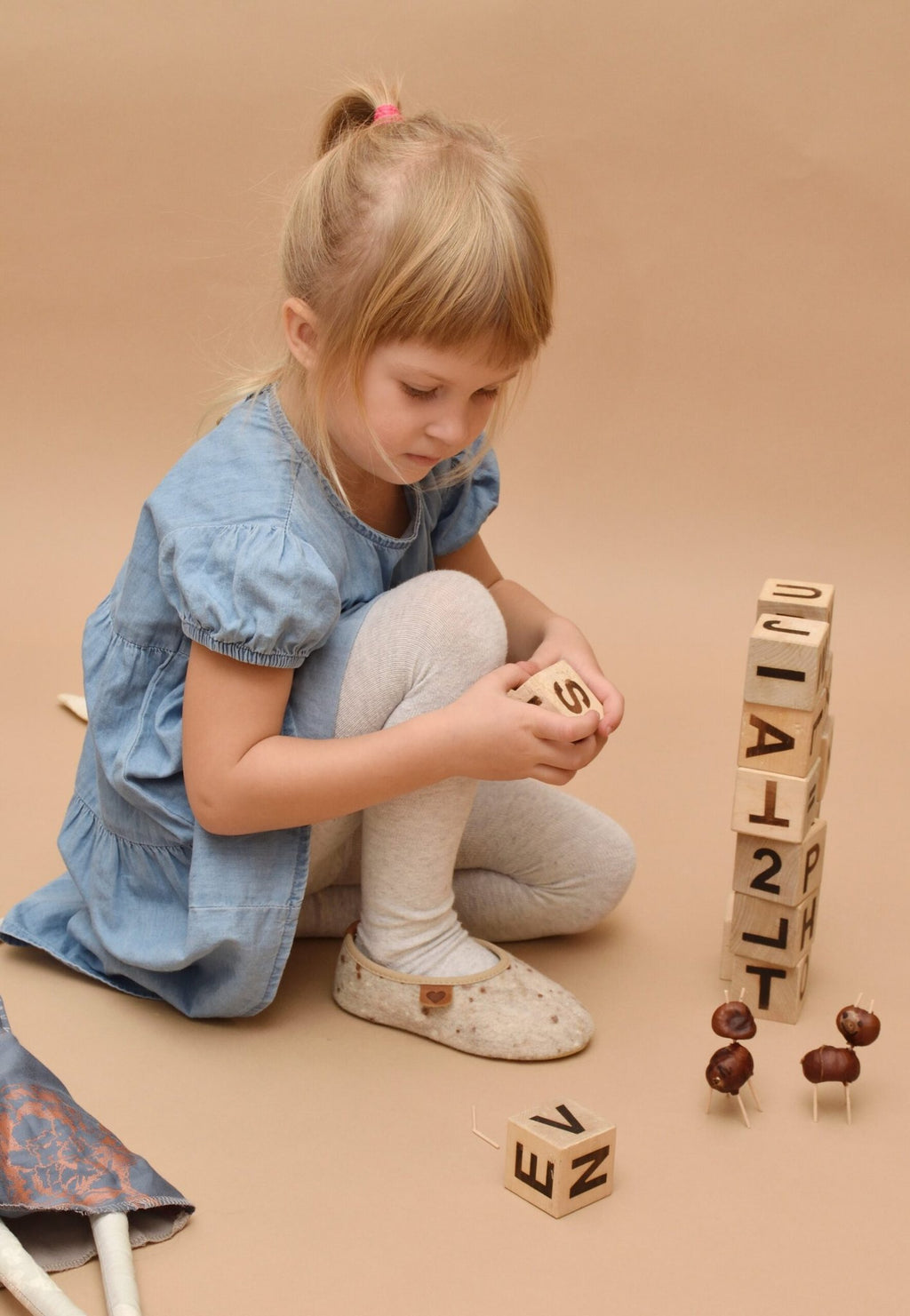 1. Girl playing with blocks wearing Omaking Kids' Slippers Põnni in natural felt, showcasing cozy indoor style