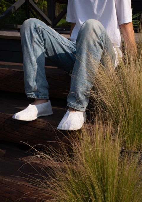 2. Unisex Tohkri slippers in white lambswool worn by a person sitting on outdoor steps