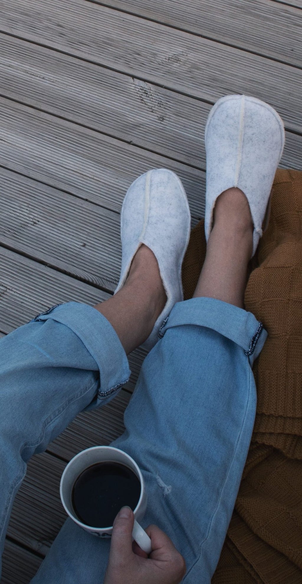 1. Unisex Tohkri slippers in white lambswool worn by a person relaxing with coffee on a wooden deck