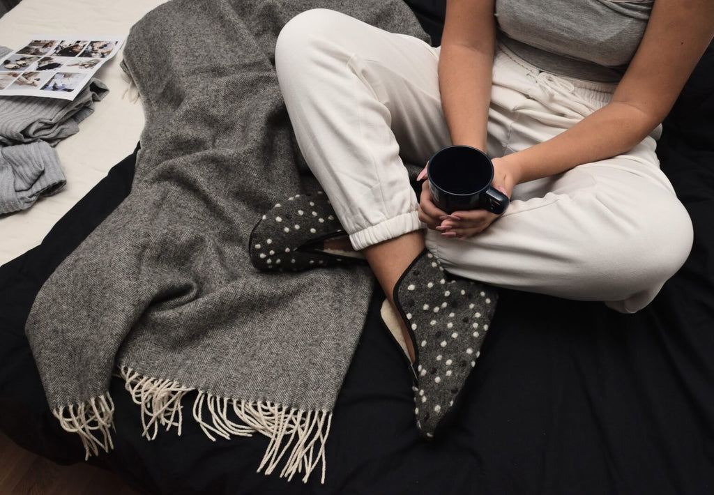 1. Woman wearing Omaking Barefoot Wool Slippers Trolla with dots, sitting on bed with blanket and holding a mug