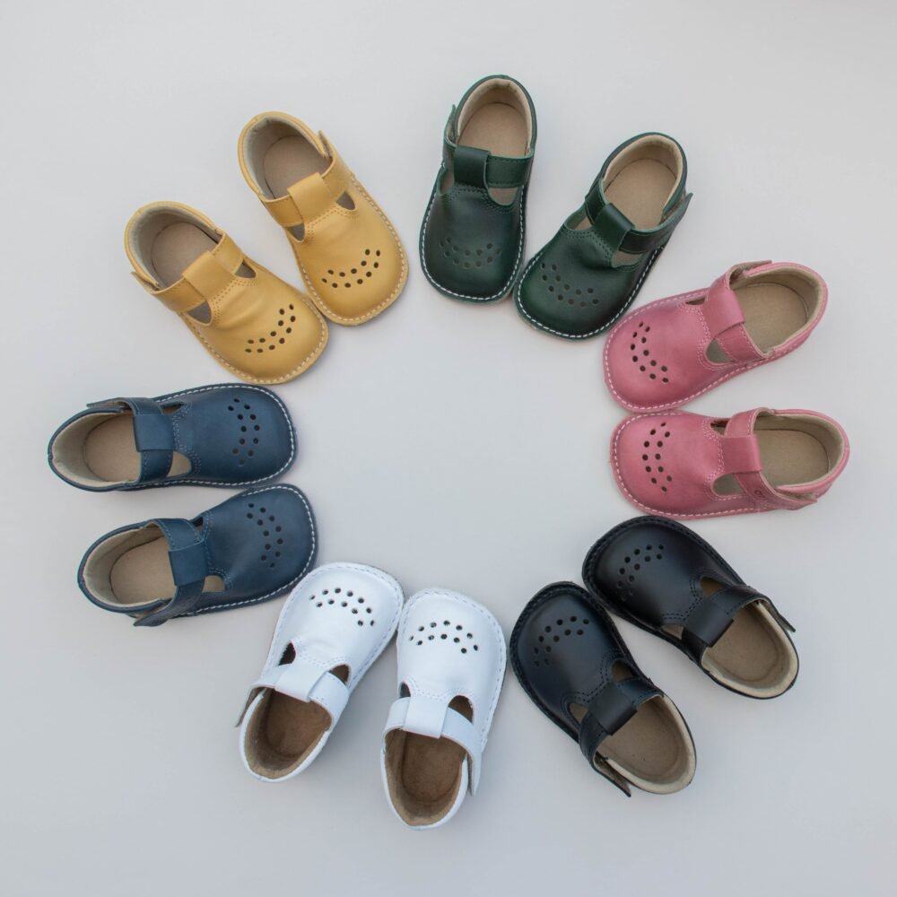 4. Assorted colors of Lusti leather kids' shoes by Omaking arranged in a circle, featuring dark green, yellow, pink, blue, white, and black