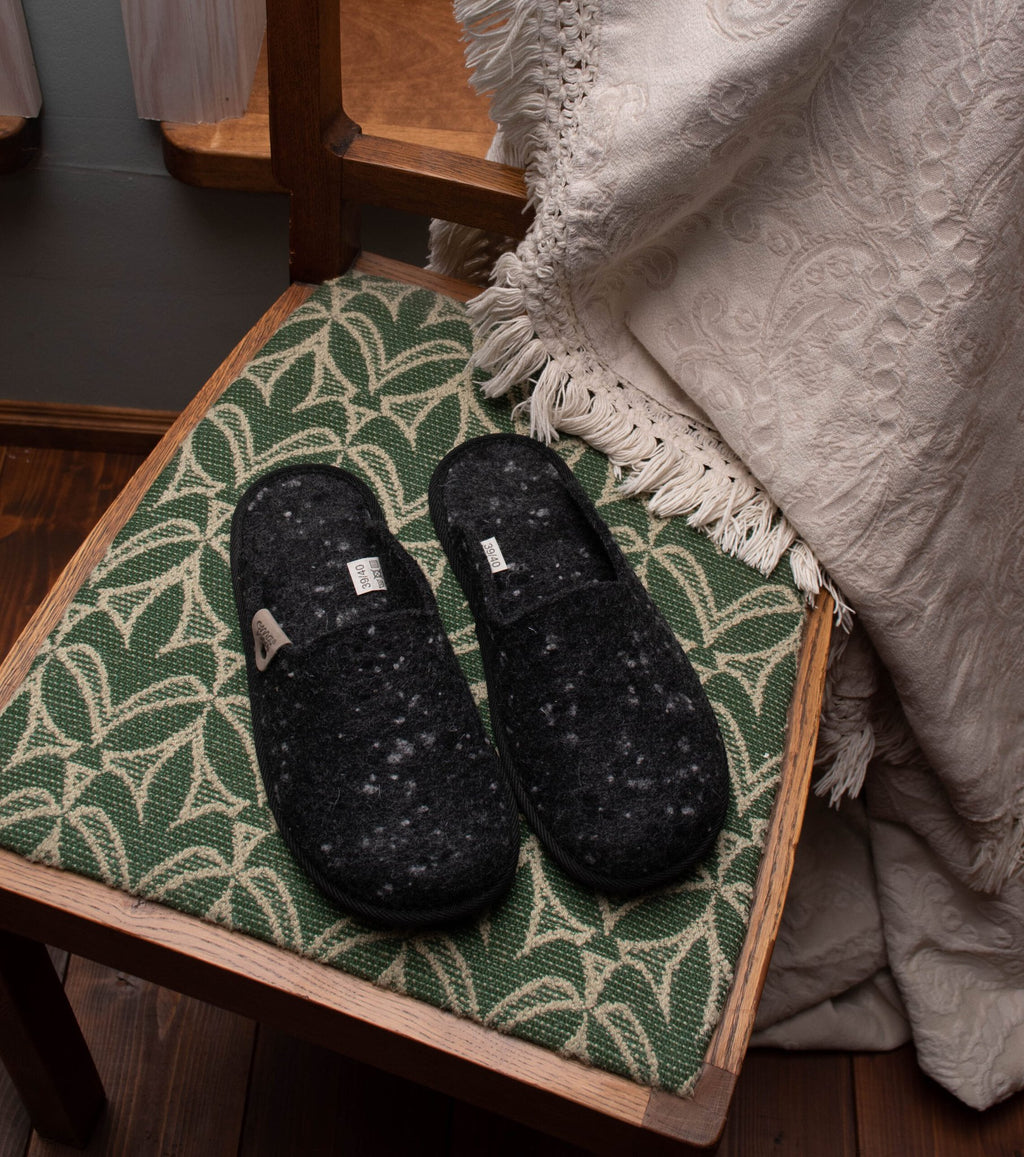 2. Omaking dark grey felt slippers placed on a patterned chair in a cozy home environment