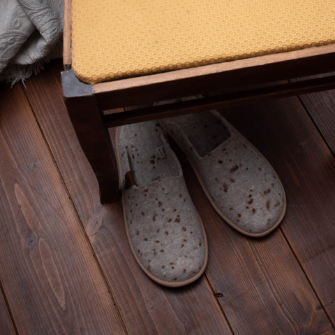 1. Lifestyle image of Omaking Pelsi beige felt slippers with dots placed under a wooden bench
