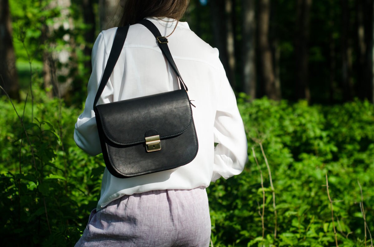 2. Woman wearing Zelma Kraft black leather saddle bag in outdoor setting, shown from front