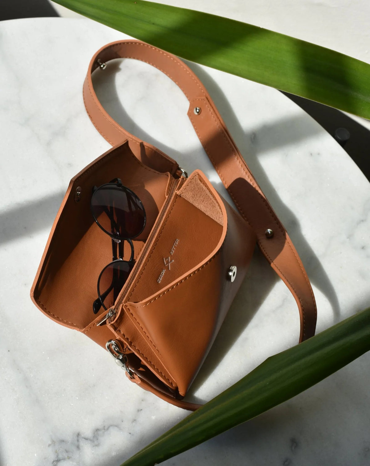9. Open brown Gerda Retter bag showing interior pockets and sunglasses on marble surface