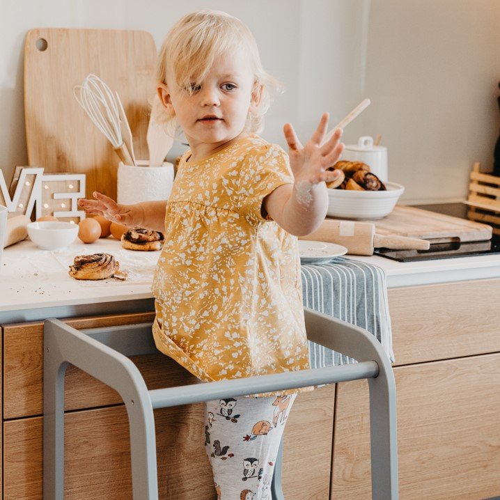3. Child in yellow top on grey Montessori helper tower step stool in kitchen