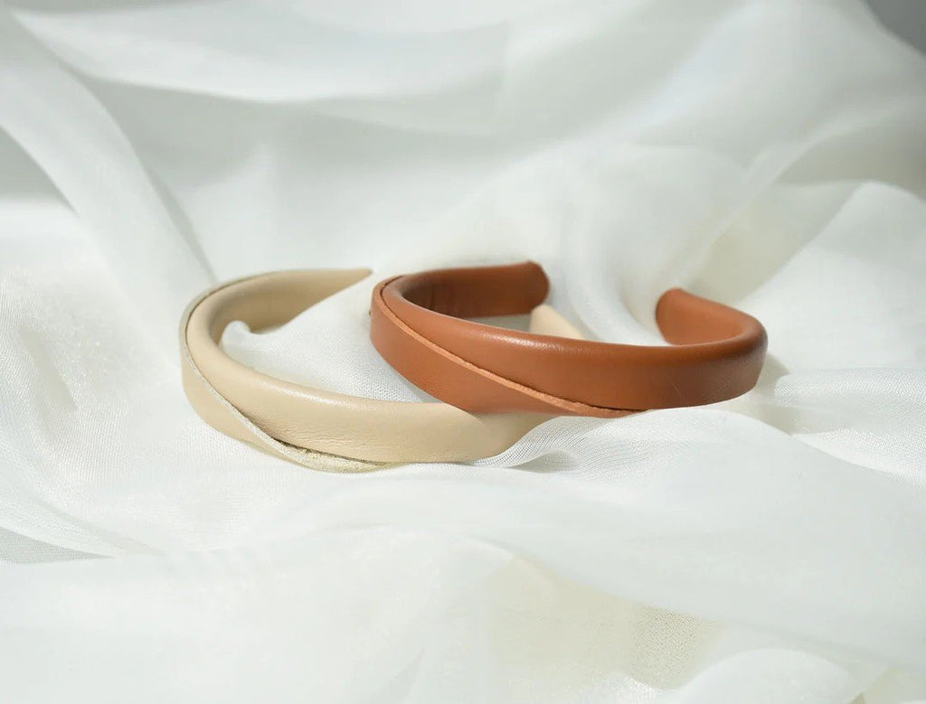 2. Close-up of beige and caramel brown handmade leather bracelets by Gerda Retter Design on white fabric, highlighting geometric elegance