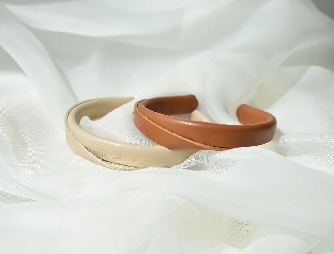 2. Close-up of beige and caramel brown handmade leather bracelets by Gerda Retter Design on white fabric, highlighting geometric elegance