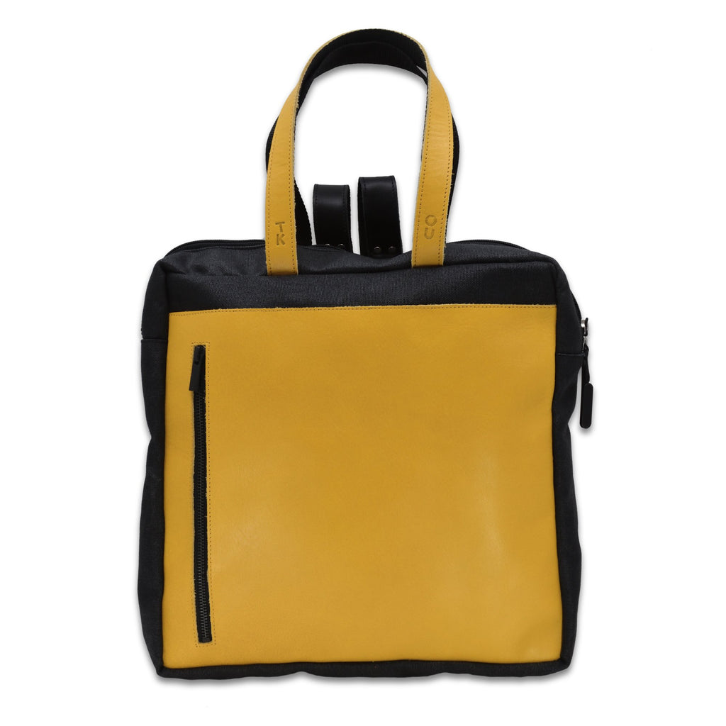 1. Omaking Stockholm Backpack in vibrant yellow with black accents, featuring leather handles and front zipper pocket, shown in studio setting
