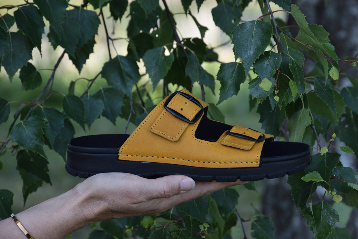 2. Meeliku Ocre Sandals by Omaking held in hand, showcasing natural leather and adjustable buckle straps, outdoor setting