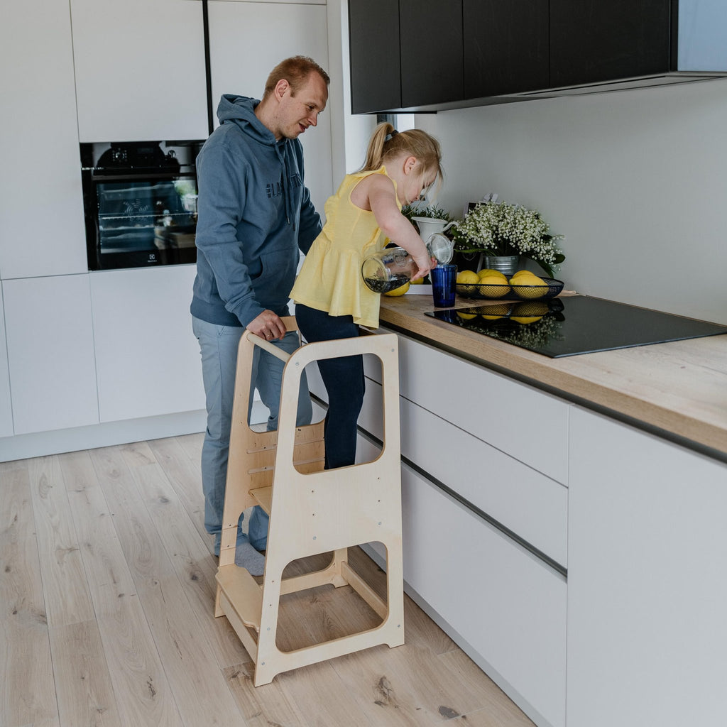 1. Man assisting child on natural wood Montessori helper tower step stool in modern kitchen