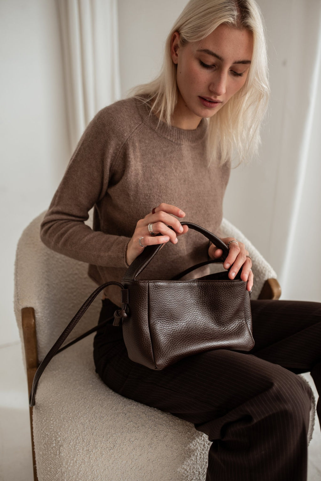 1. Woman holding Lava flow Crossbody Bag MERU in dark brown leather, seated in a cozy setting
