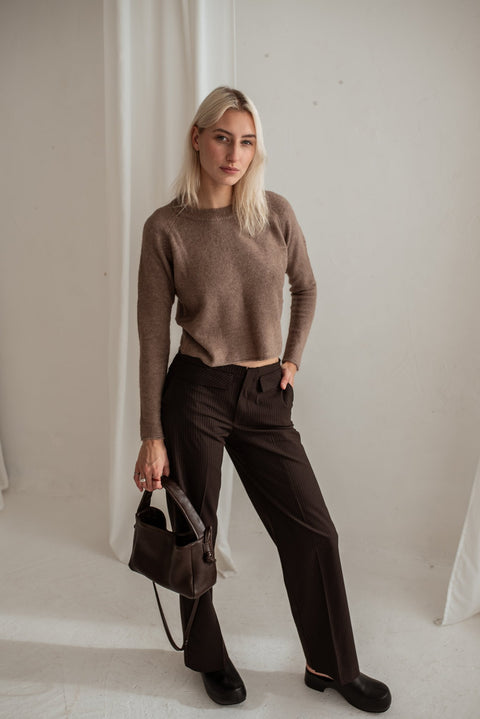 2. Woman standing with Lava flow Crossbody Bag MERU in dark brown leather, showcasing versatile style