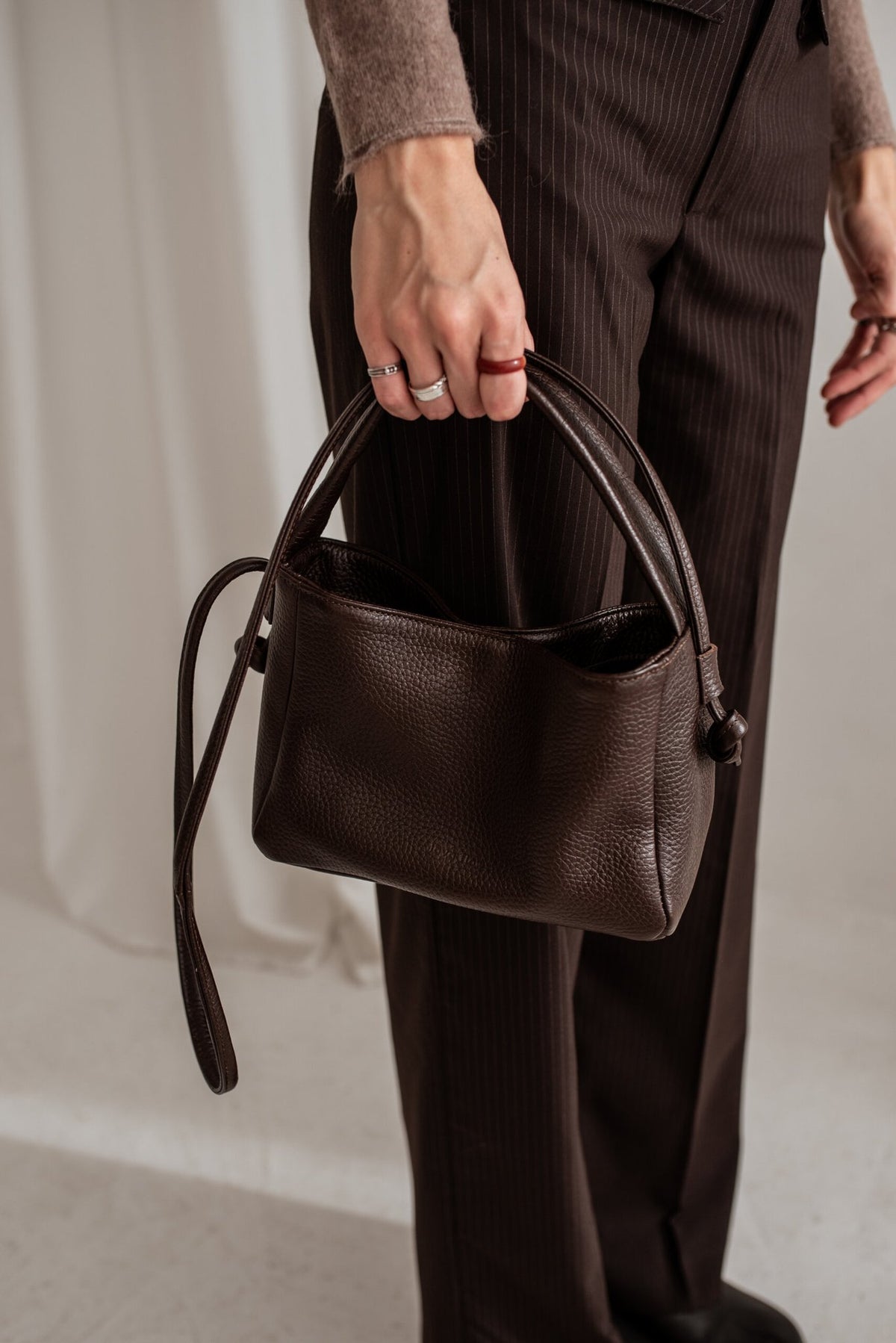 3. Close-up of Lava flow Crossbody Bag MERU in dark brown leather, held by a woman