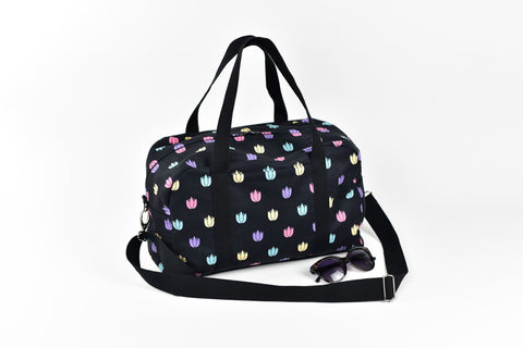 1. Garbanota travel bag with colored tulips pattern, featuring long strap and exterior pocket, shown with sunglasses in studio setting