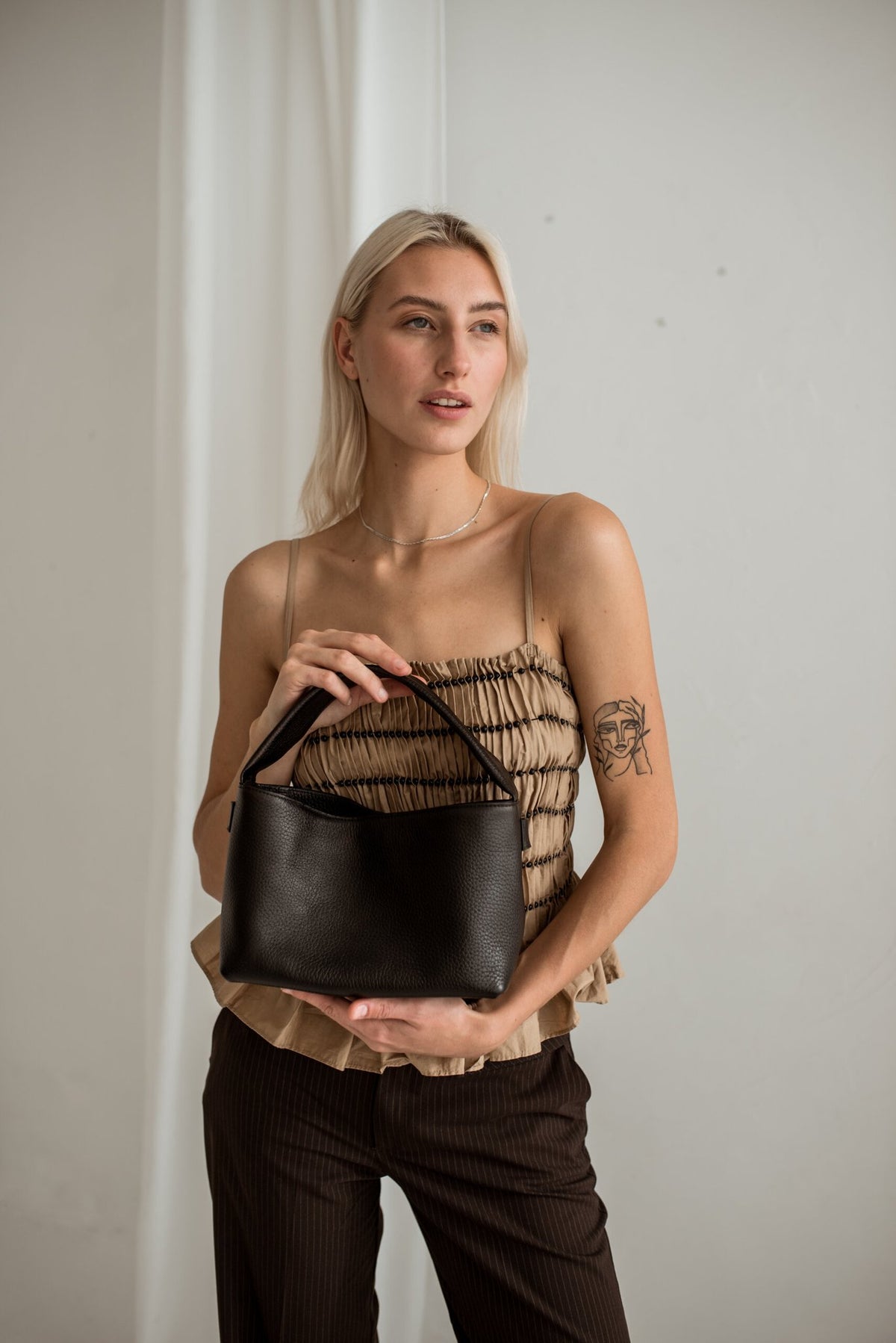 1. Woman holding Lava Flow Crossbody Bag MERU in black, showcasing minimalist design and Italian leather