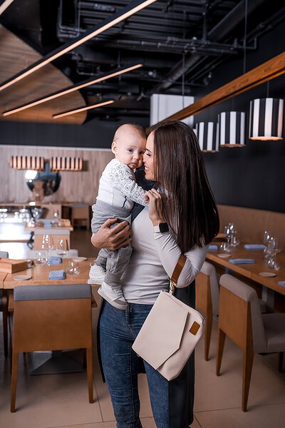 3. Woman holding baby with Ally Scandic Älly Handbag in Cappuccino, emphasizing practicality and style in lifestyle setting