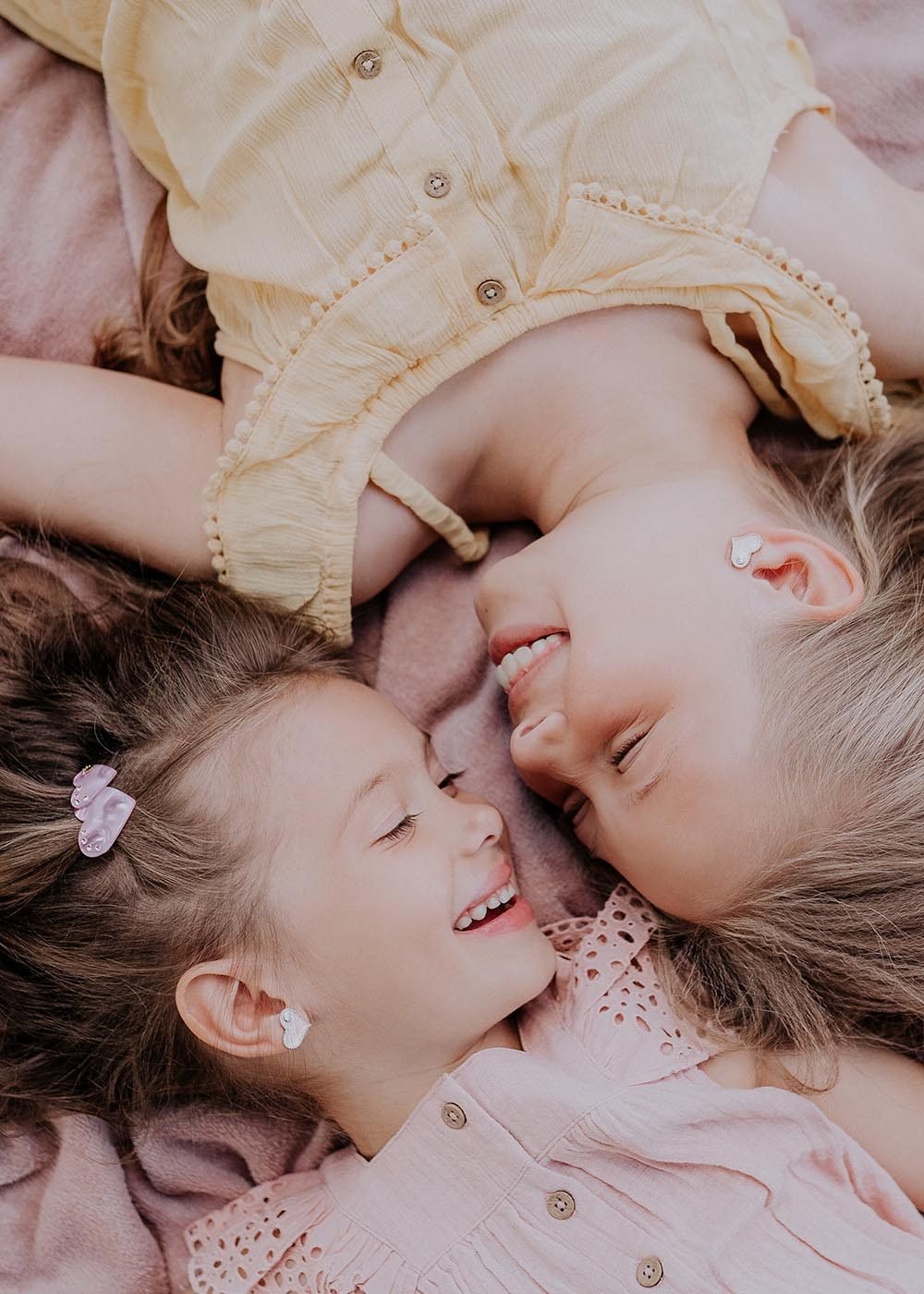 1. Two young girls wearing Dondella white heart earrings with zircon stones, lying on a blanket, showcasing the earrings' elegance and charm