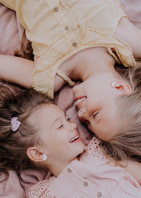 1. Two young girls wearing Dondella white heart earrings with zircon stones, lying on a blanket, showcasing the earrings' elegance and charm