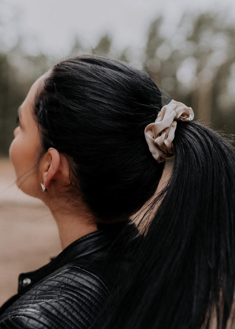 1. Woman wearing Dondella luxury silk scrunchie in beige, styled in a ponytail outdoors
