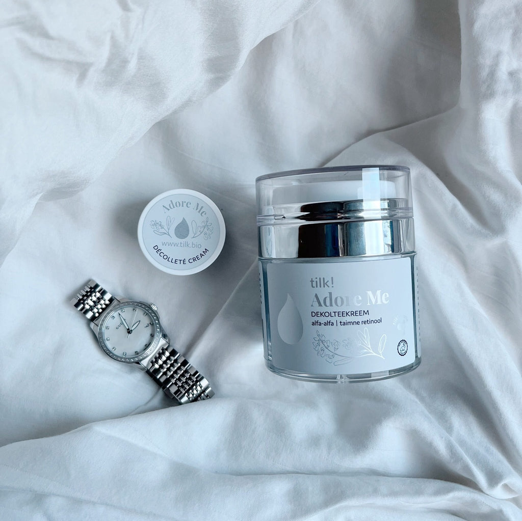 1. Lifestyle image of Tilk! Adore Me Rich Décolleté Cream with alfalfa and plant-based retinol, shown with a watch on a white fabric background
