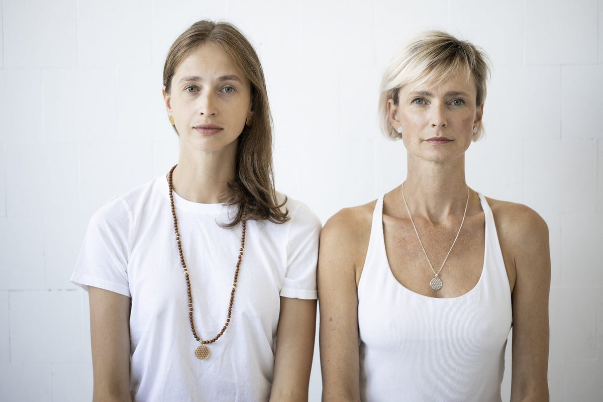 1. Two women wearing New Vintage by Kriss Flower Of Life necklaces in silver and gold, showcasing unisex design