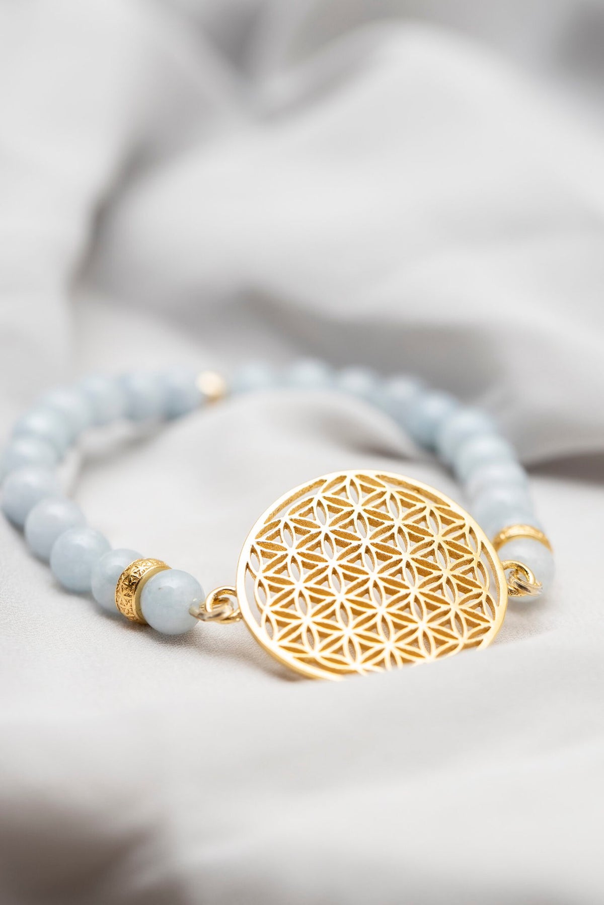 3. Close-up of New Vintage by Kriss Flower Of Life Bracelet in aquamarine with gold-plated silver medallion on soft fabric