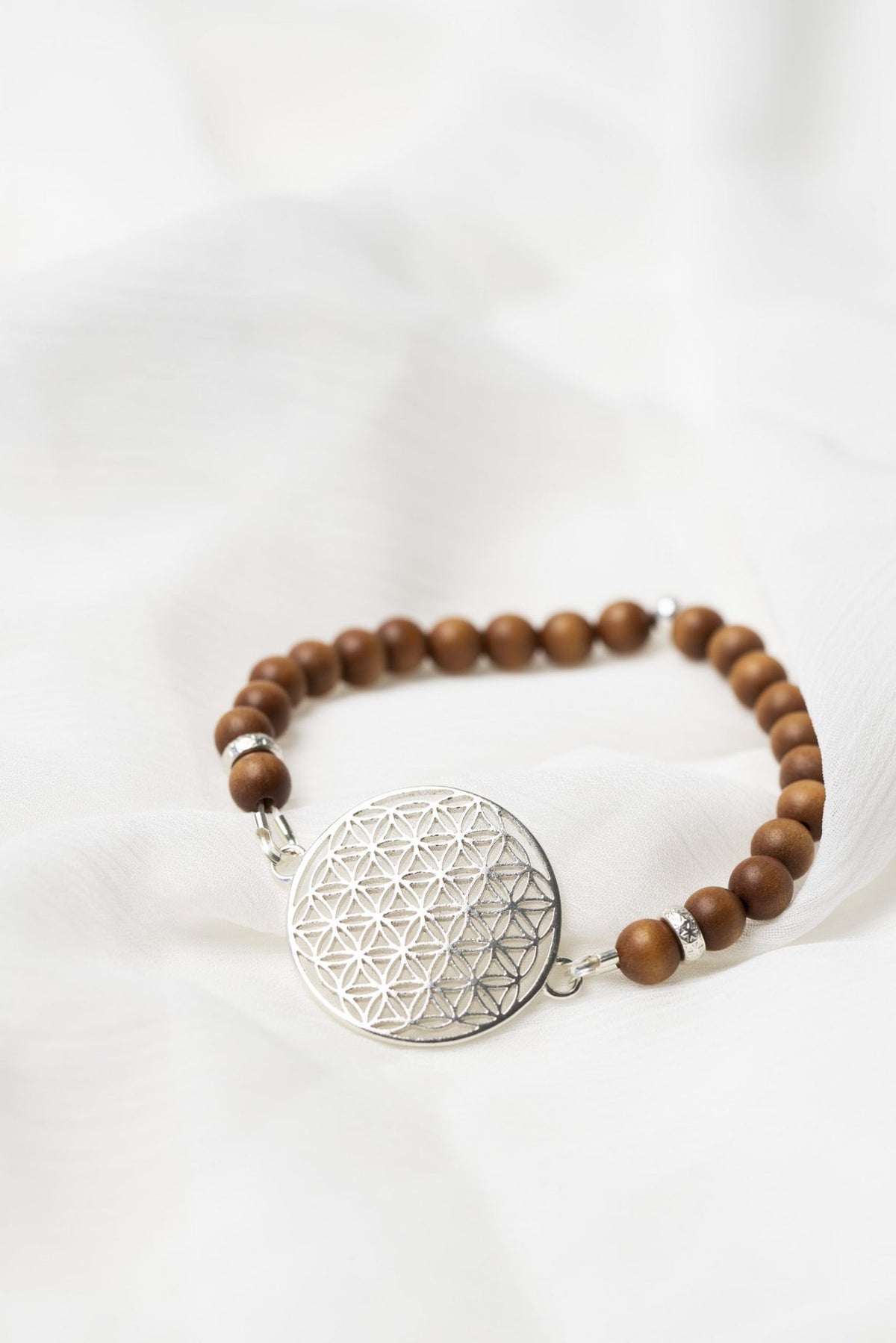 7. Close-up of New Vintage by Kriss Flower Of Life Bracelet in sandalwood with 925 silver medallion on white fabric