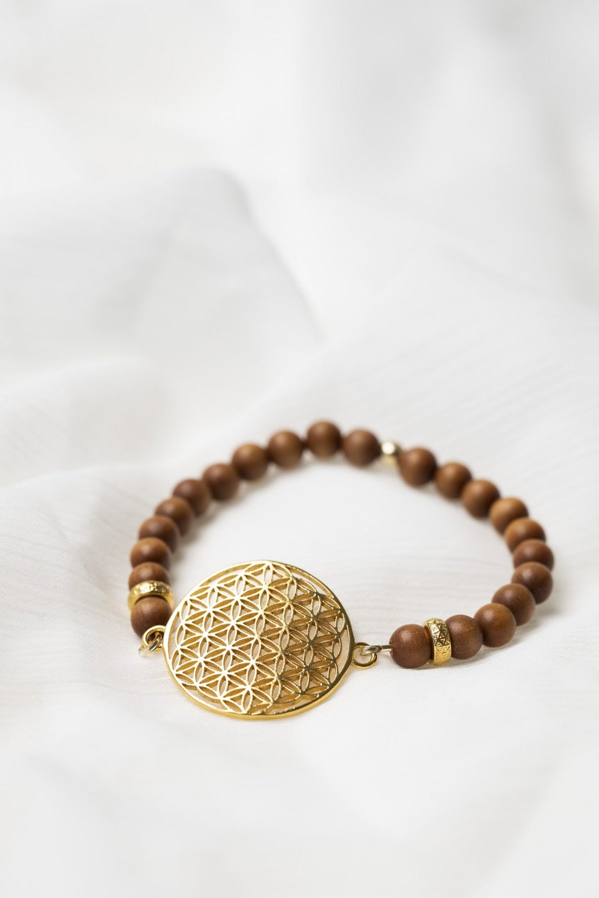 6. Close-up of New Vintage by Kriss Flower Of Life Bracelet in sandalwood with gold plated silver medallion on white fabric
