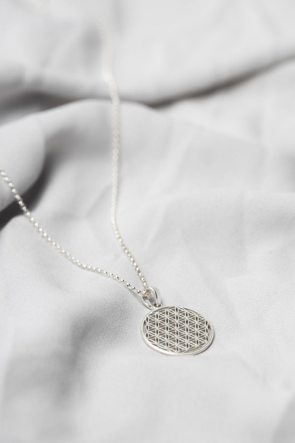 6. Close-up of New Vintage by Kriss Flower Of Life necklace in silver on fabric, highlighting 3D printed design