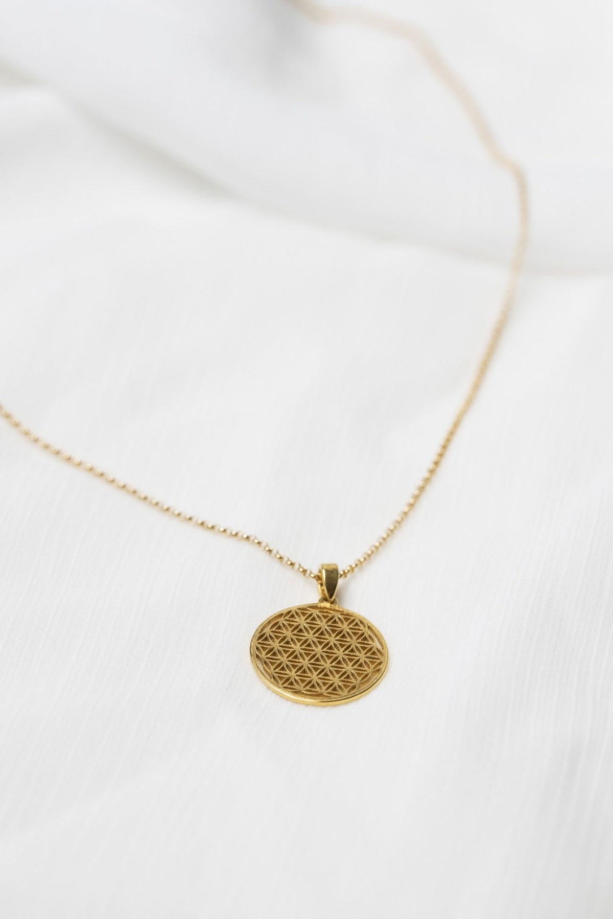 7. Close-up of New Vintage by Kriss Flower Of Life necklace in gold on fabric, emphasizing sacred geometry pattern
