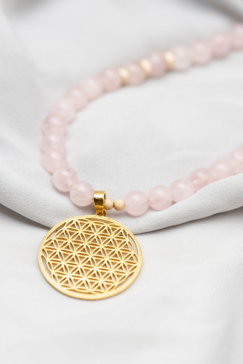 1. Close-up of New Vintage by Kriss Flower Of Life Bracelet in rose quartz with gold plated silver pendant on fabric