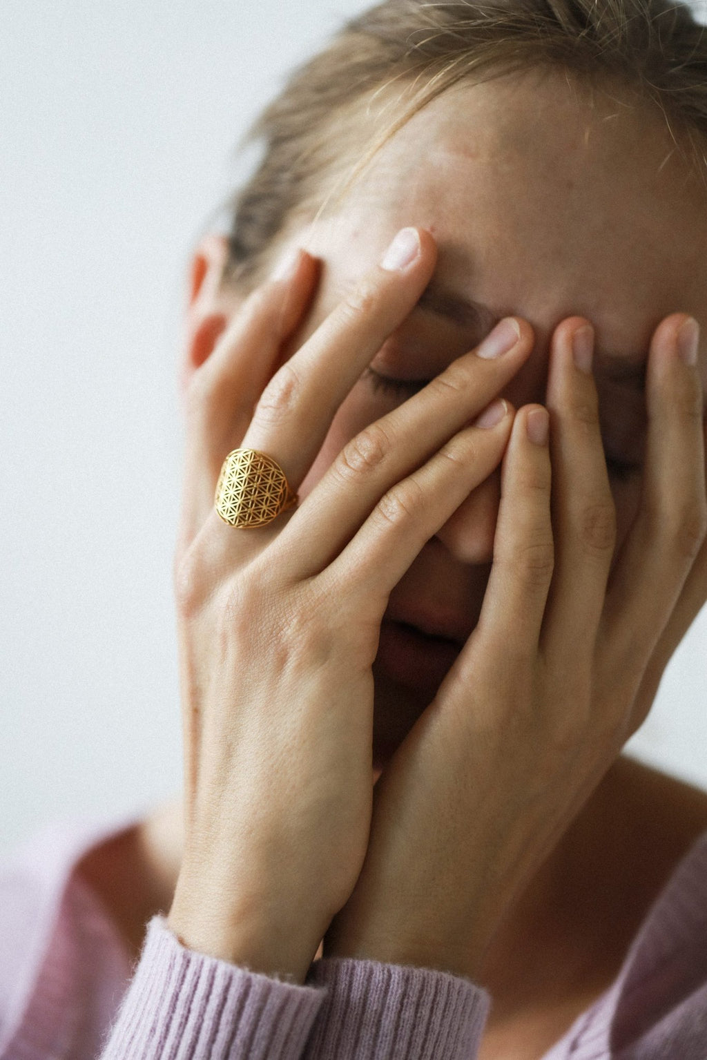 6. Woman covering face with hands, wearing gold Flower Of Life Ring, highlighting its bold design