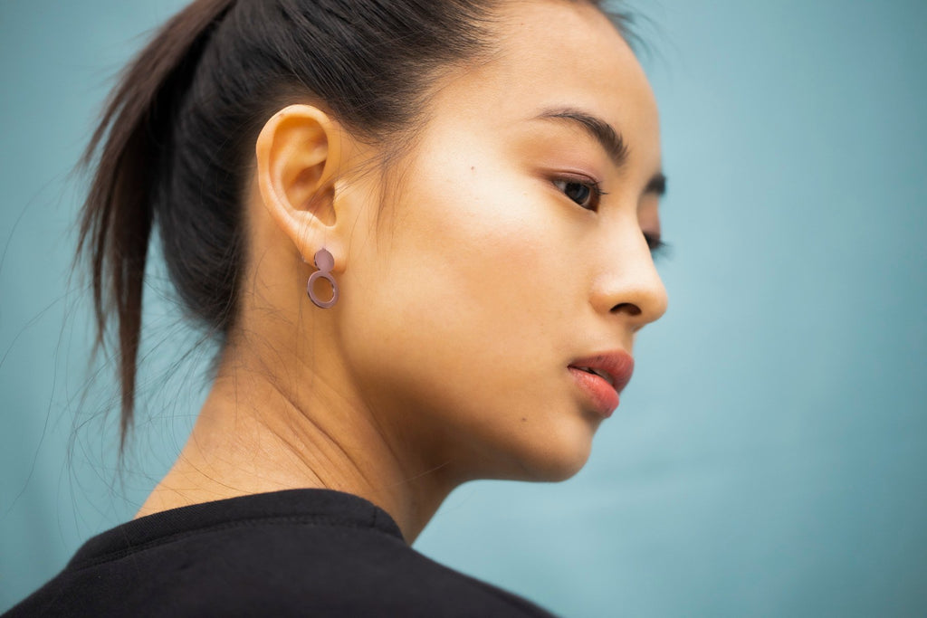 1. Woman wearing Lentsius Arc Purple earrings, showcasing Scandinavian design against a blue background