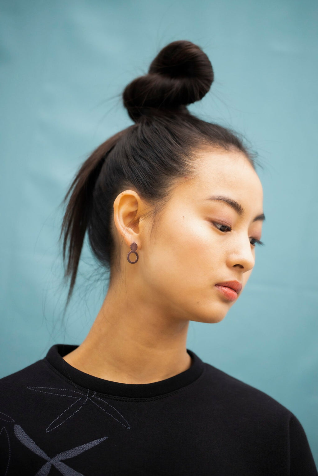 6. Woman with Lentsius Arc Purple earrings, styled with a top bun, against a blue background