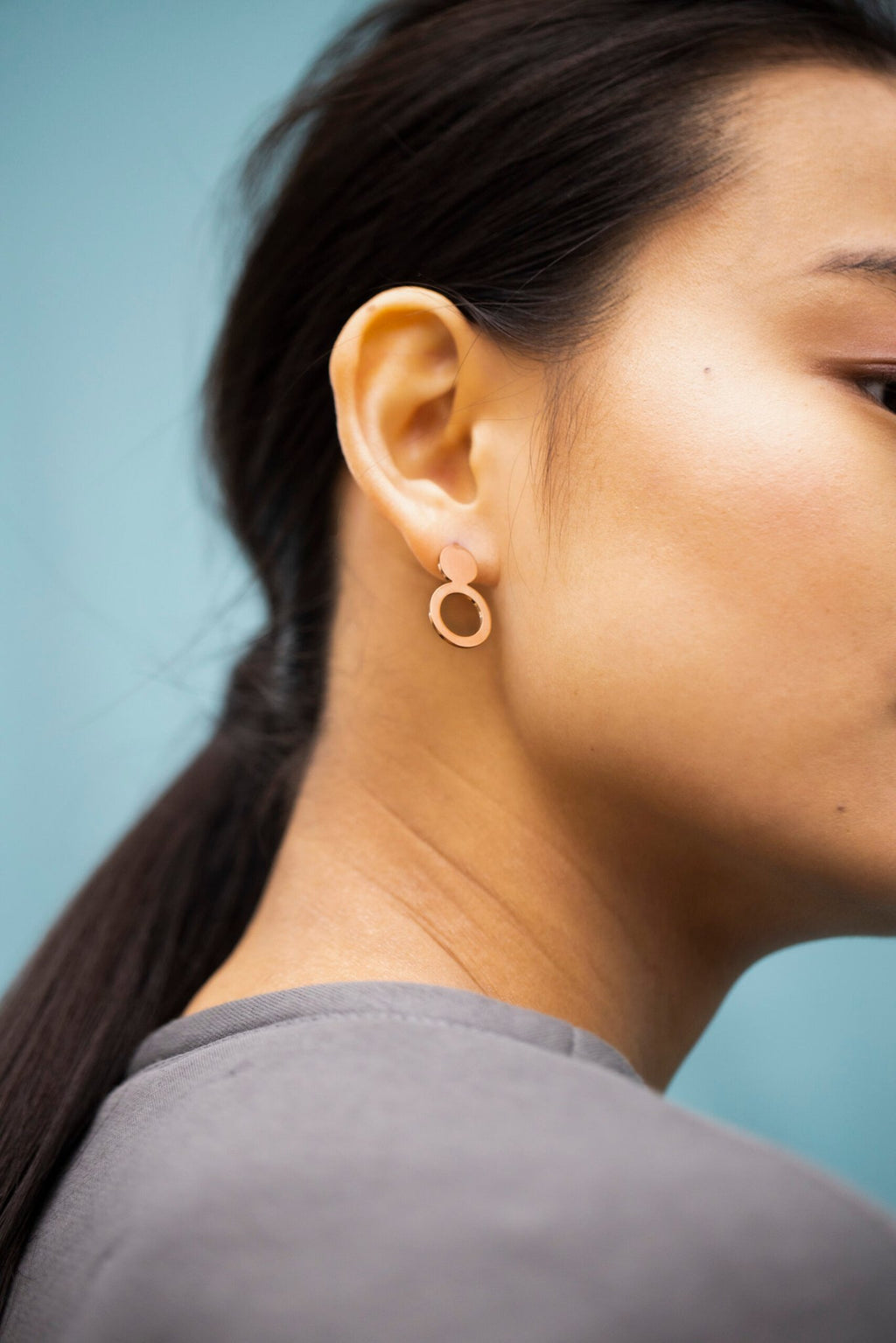 1. Woman wearing Lentsius Arc rose gold earrings, showcasing Scandinavian style against a blue background