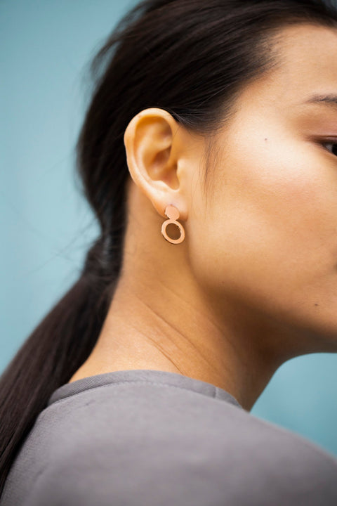 1. Woman wearing Lentsius Arc rose gold earrings, showcasing Scandinavian style against a blue background