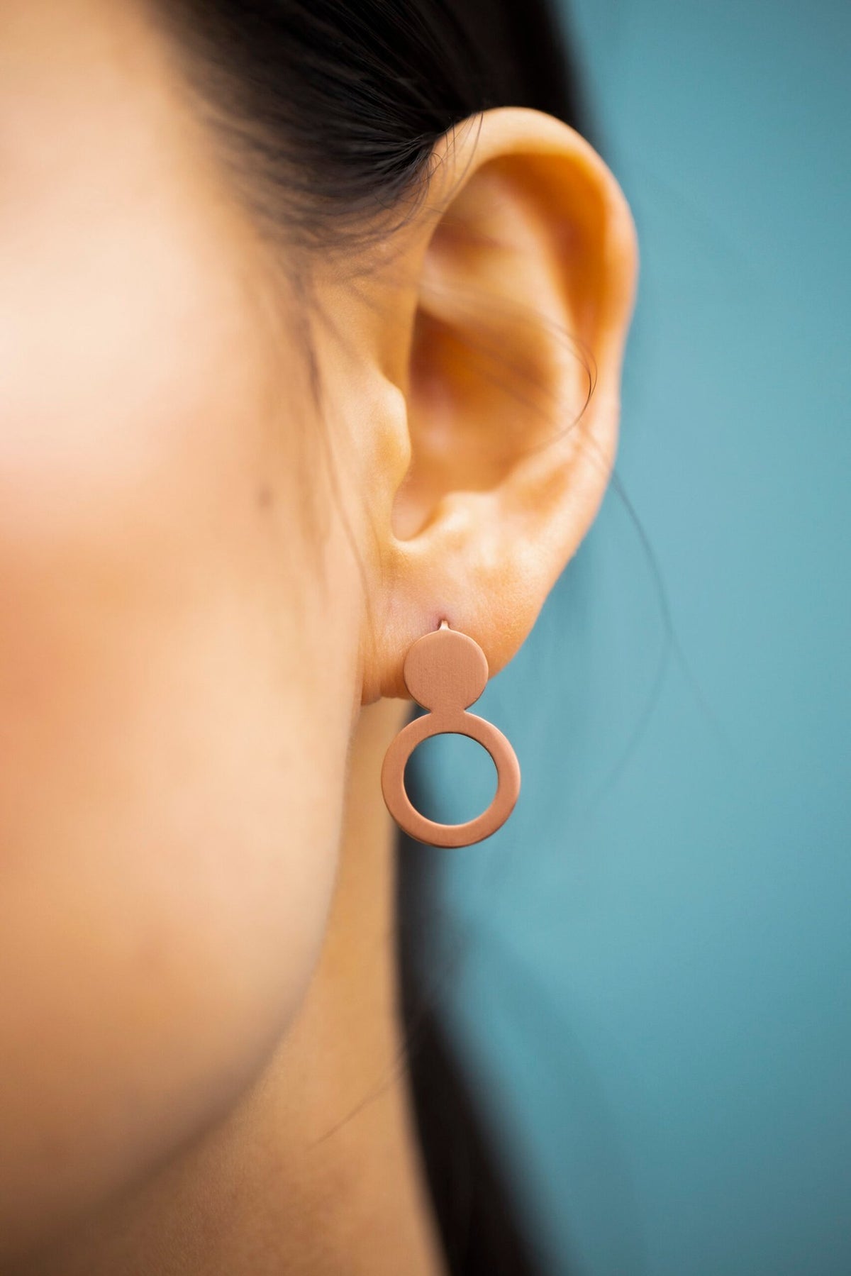 6. Close-up of Lentsius Arc rose gold earrings, showing brushed surface finish and silicone stoppers