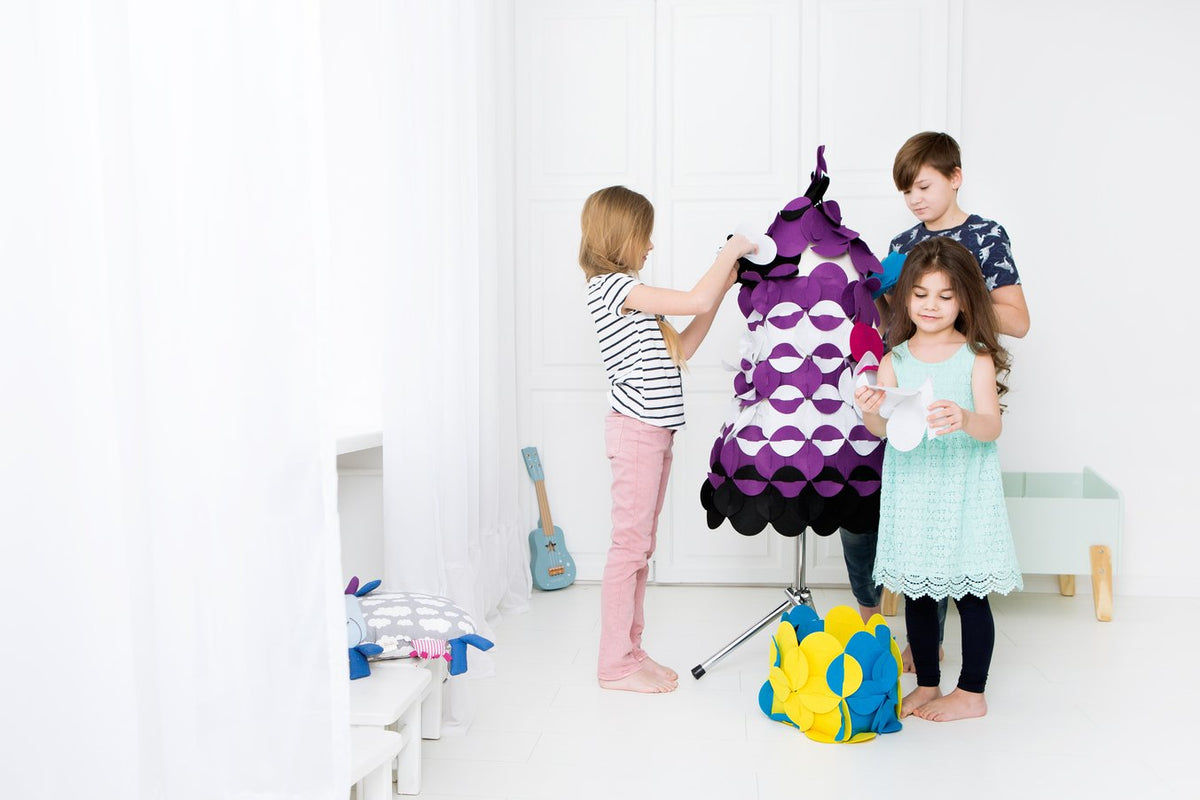 1. Three children assembling a purple and black felt costume on a mannequin in a bright room