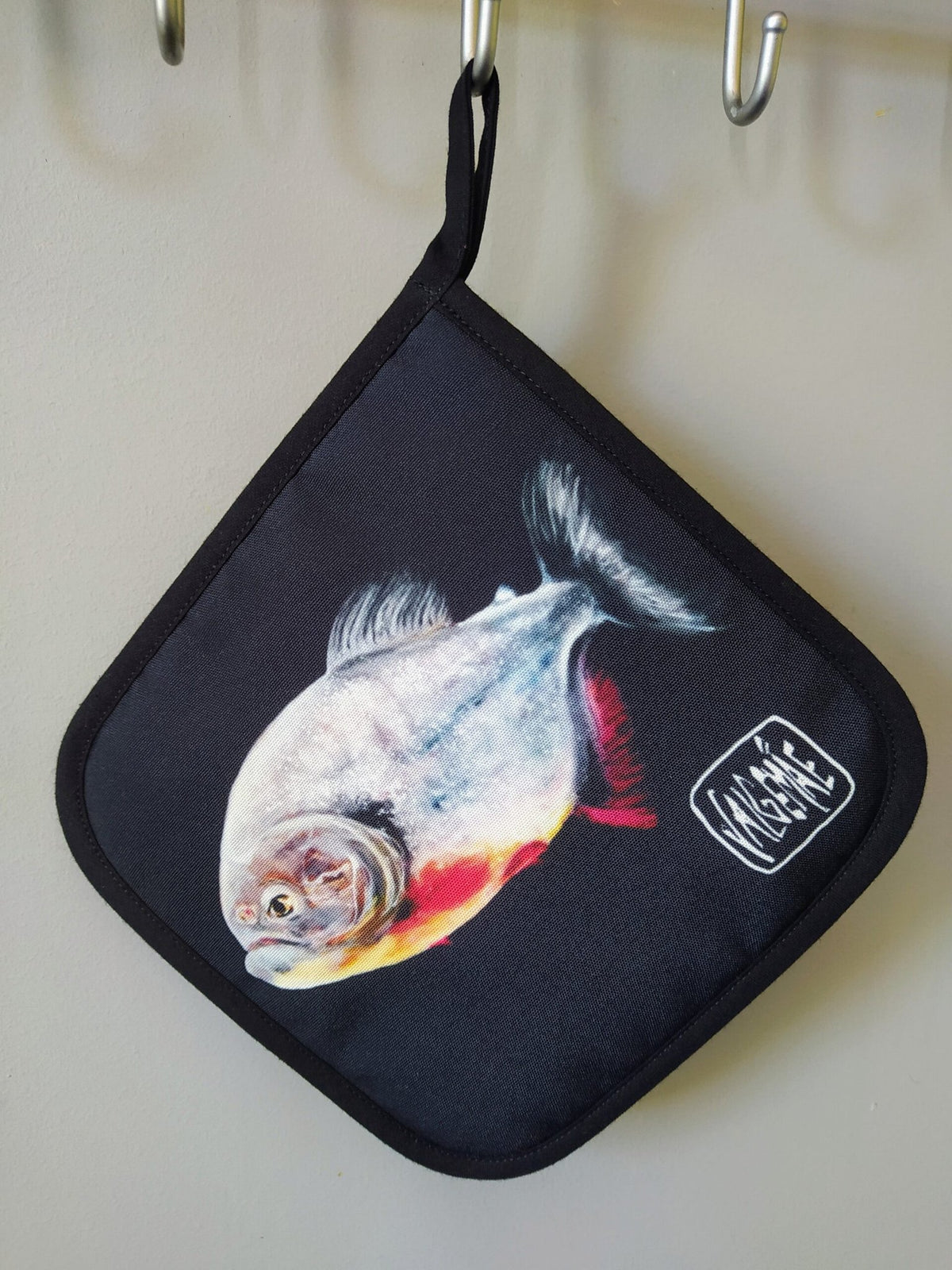 3. Pot holder with fish painting inspired by Goya, hanging on a hook, featuring a dark background and artist's signature