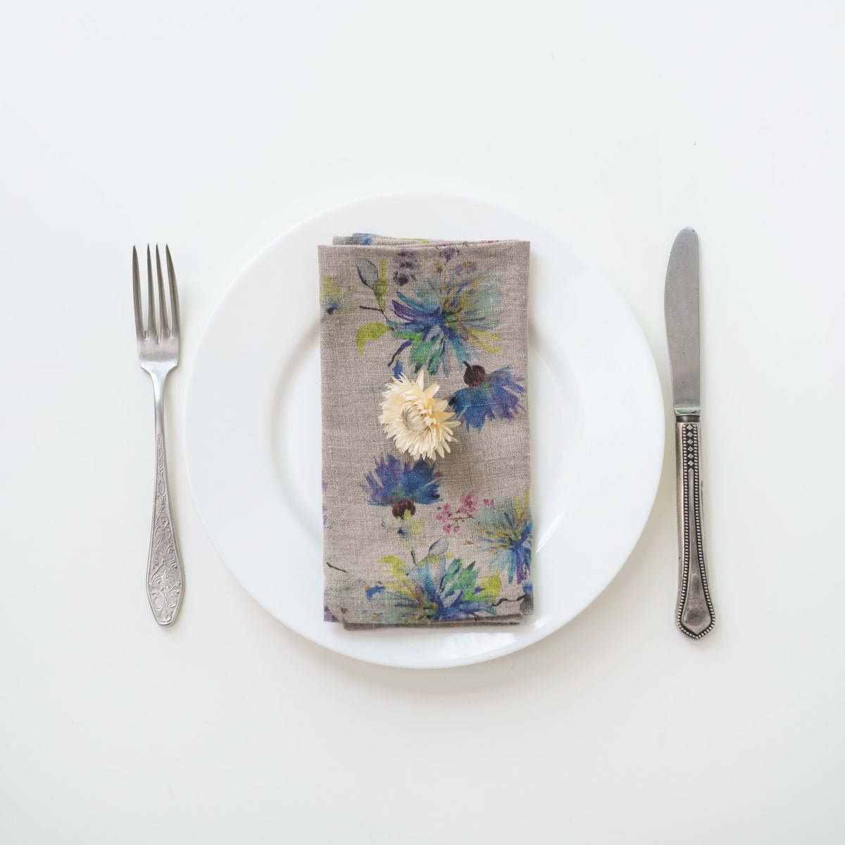11. Floral linen napkin on a white plate with a decorative flower, accompanied by fork and knife