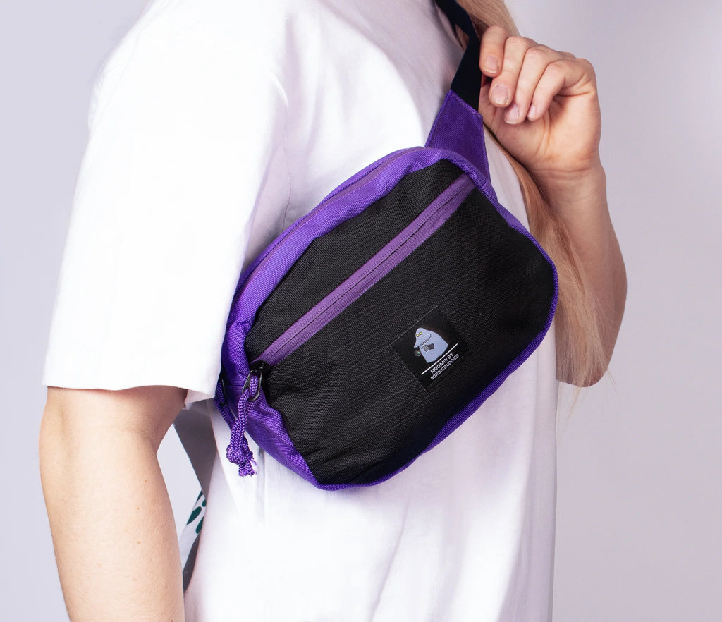 1. Woman wearing The Groke Retro Waist Bag in black and purple by Moomin, shown in lifestyle setting