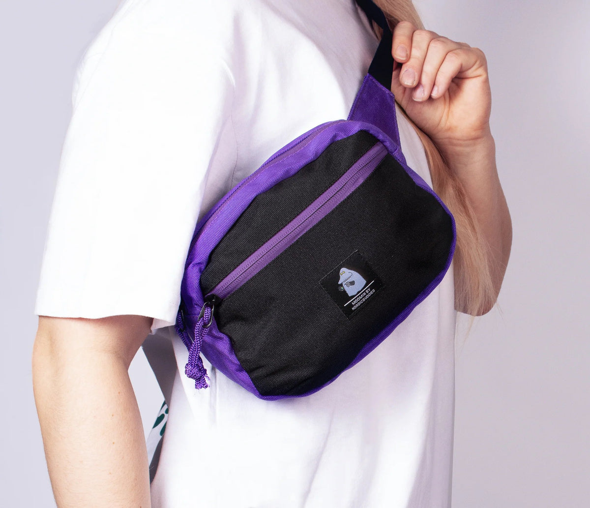1. Woman wearing The Groke Retro Waist Bag in black and purple by Moomin, shown in lifestyle setting