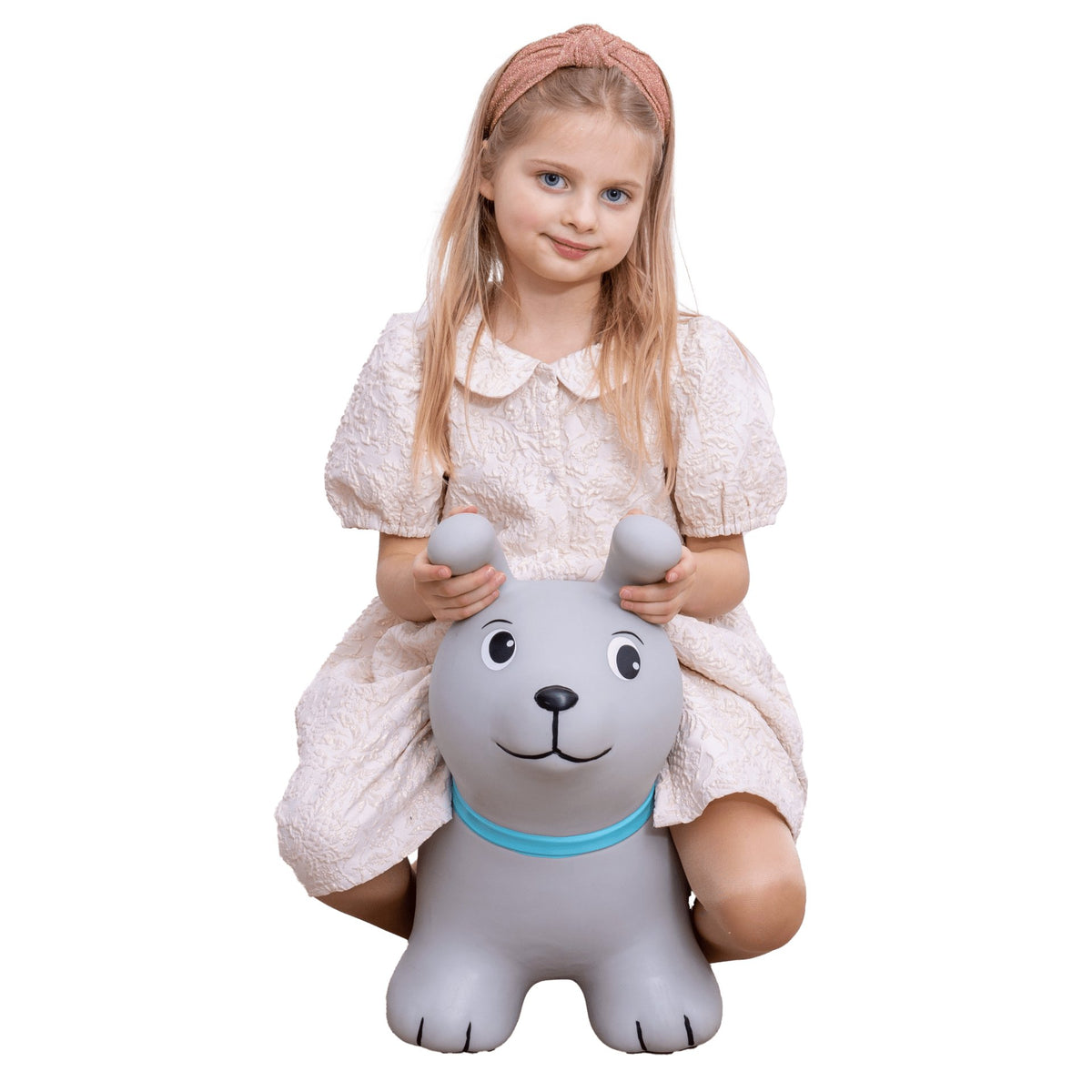 1. Young girl sitting on grey dog-shaped hopper toy with blue collar, wearing a light dress, against a black background