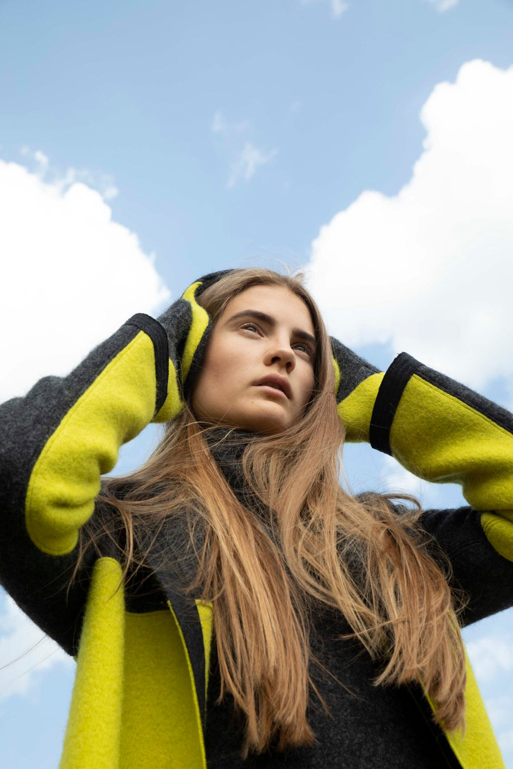 1. Woman wearing HERTTA felted wool earmuffs in dark grey and apple green, styled with matching coat, outdoor lifestyle setting