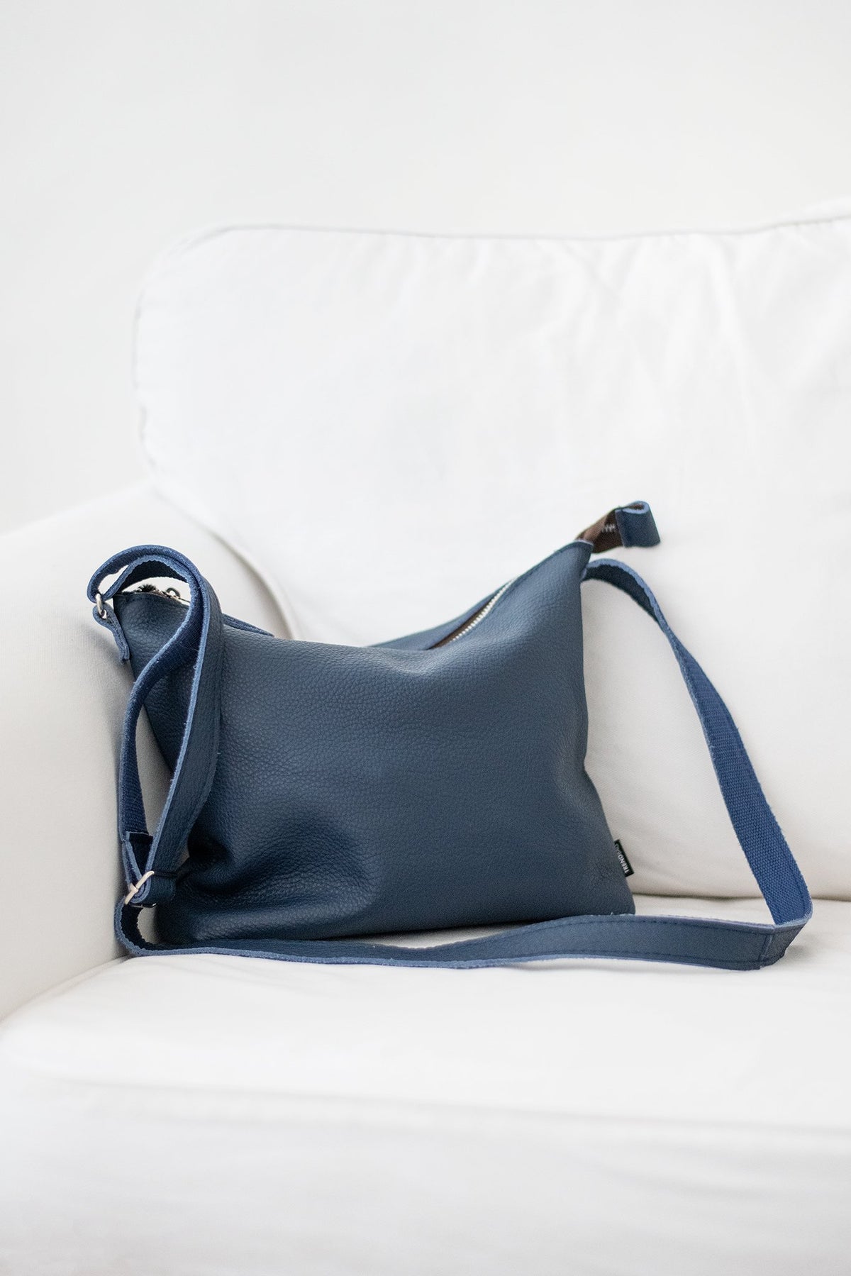 2. Dark blue Anet L shoulder bag by Trendbag, displayed on a white couch, showcasing sustainable craftsmanship