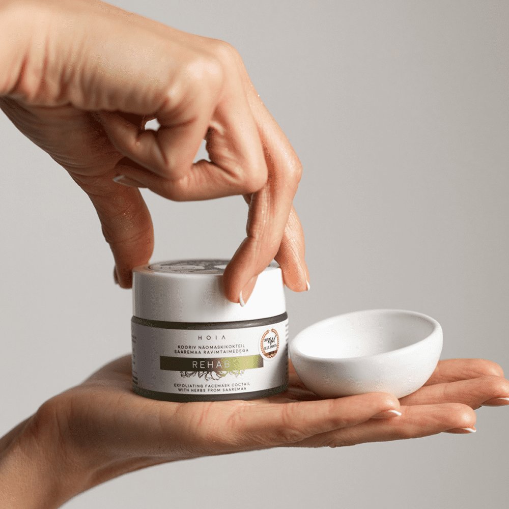 2. Hands holding HOIA homespa Rehab Exfoliating Face Mask 50ML with small bowl, showcasing product texture and packaging