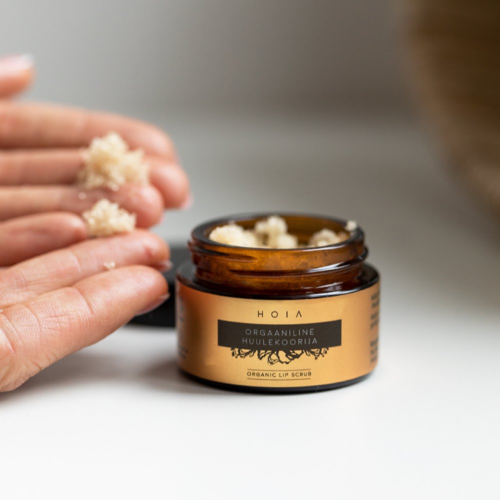 2. Close-up of HOIA homespa organic lip scrub in jar with hands applying product
